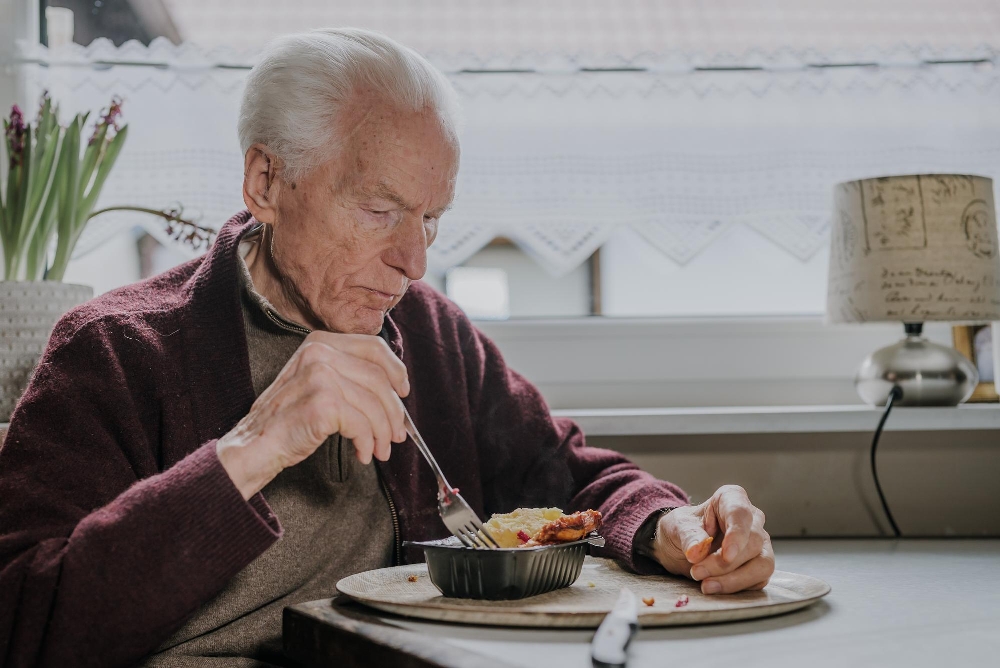 Older man in a maroon cardigan eating with a fork, illustrating Parkinson's and swallowing